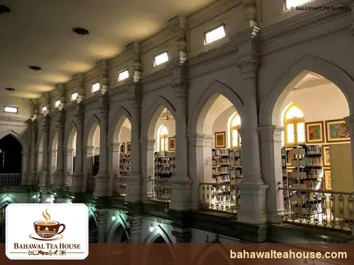 Upper gallery arches and bookshelves lit at night in Bahawalpur library